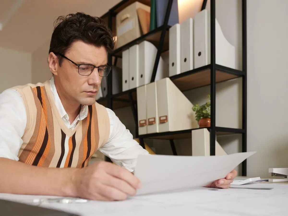 Professionnel relisant des documents techniques à son bureau devant des classeurs d'archives